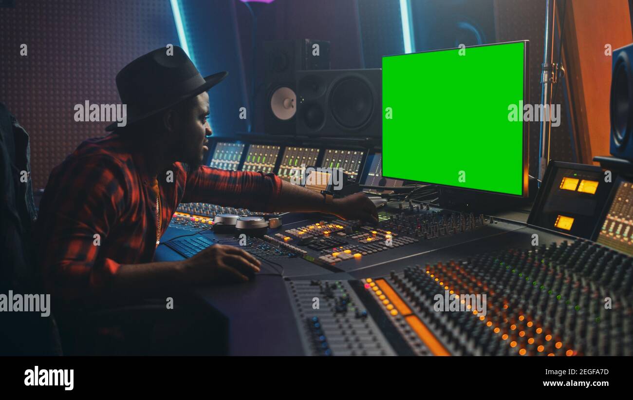 Elégant producteur d'ingénieur audio travaillant dans Music Record Studio, utilise l'écran vert Chroma Key Computer Display, l'égaliseur de carte de mixage et le pupitre de commande Banque D'Images