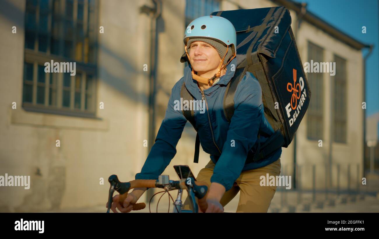 Livraison de nourriture Courier porter le sac à dos thermique fait un vélo sur la route pour livrer des commandes pour les clients et les clients. Journée ensoleillée dans la ville moderne avec Banque D'Images