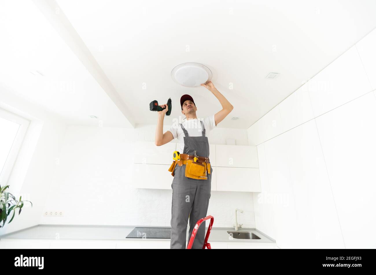 Un électricien installe un lustre au plafond. Concept de construction Banque D'Images
