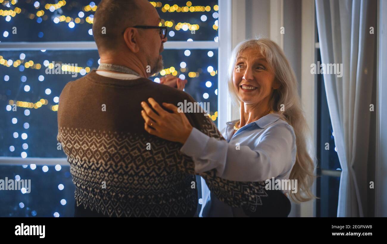Heureux couple Senior en amour ont une soirée romantique, dansant dans la cuisine, célébrant l'anniversaire. Soirée romantique avec vin, table festive à l'intérieur Banque D'Images
