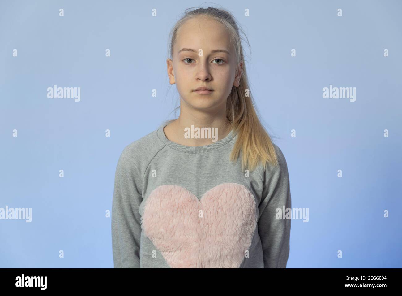 belle adolescente avec cheveux blonds dans un chemisier gris sur fond bleu. haute qualité Banque D'Images