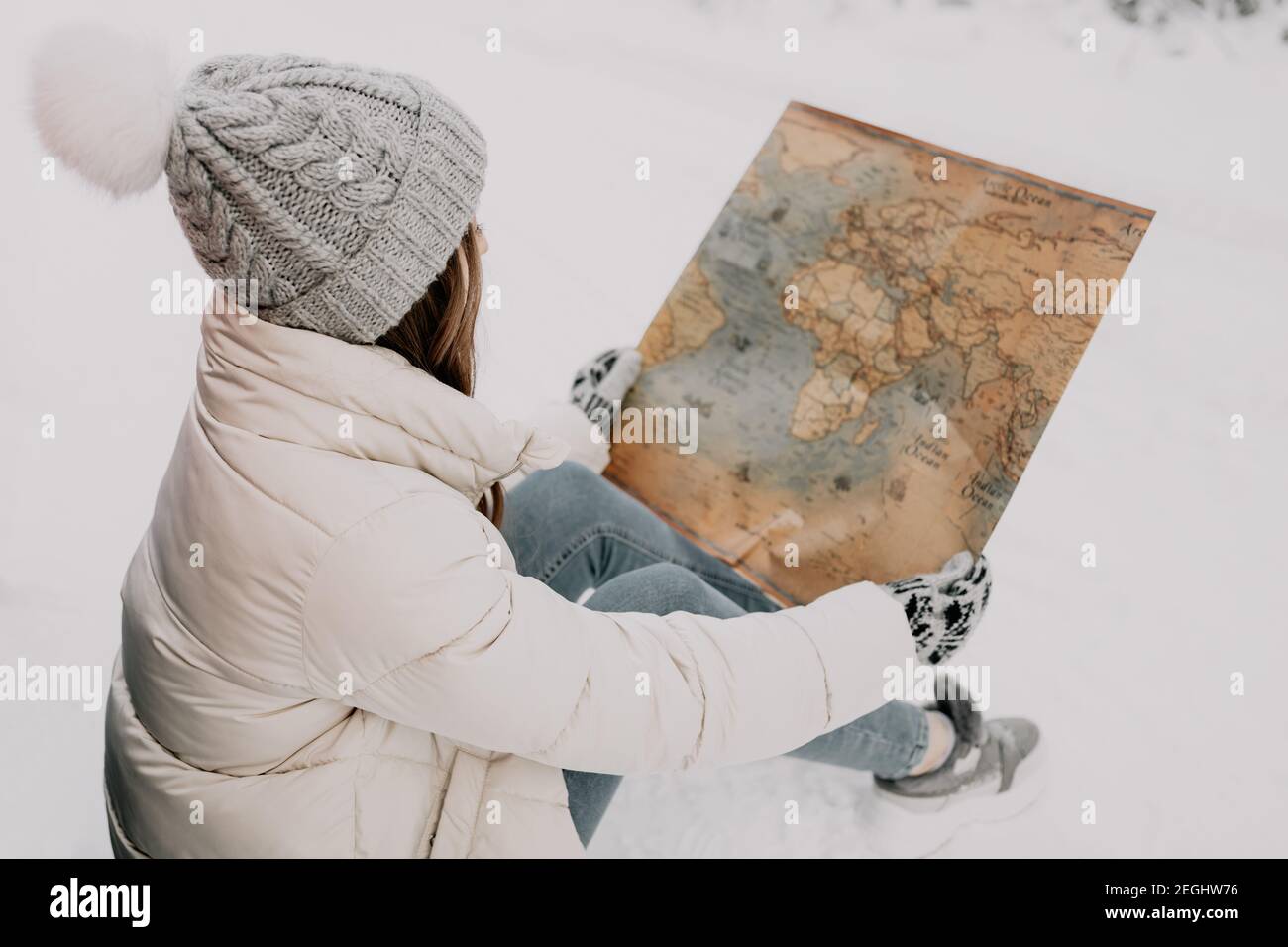Une jeune femme est assise dans la neige et tient une carte entre ses mains. Concept de voyage. Banque D'Images