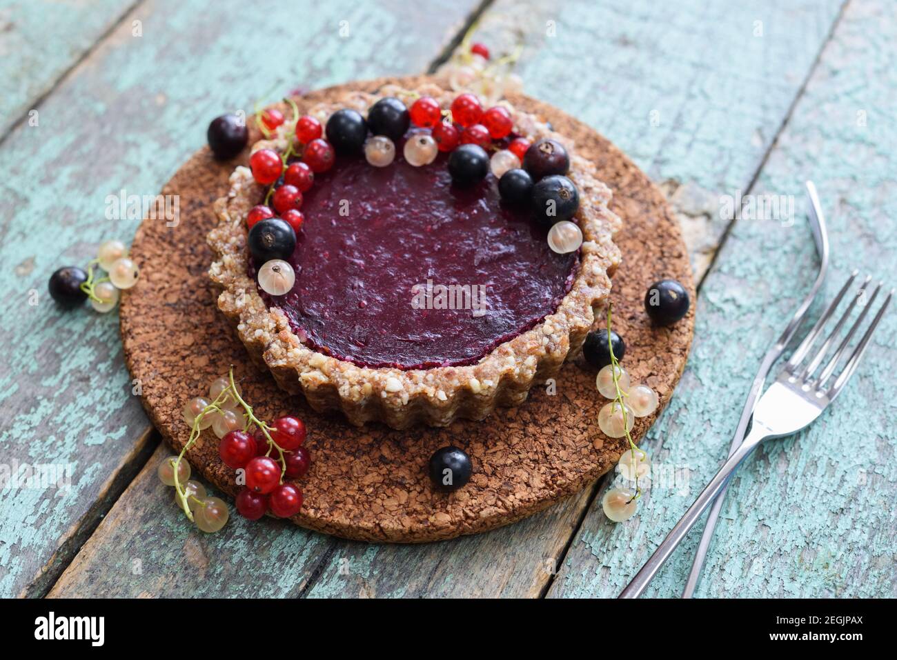Petites tartes végétaliennes faites de noix et de confiture de baies décorées de raisins de Corinthe noirs, rouges et blancs sur un panneau en liège Banque D'Images