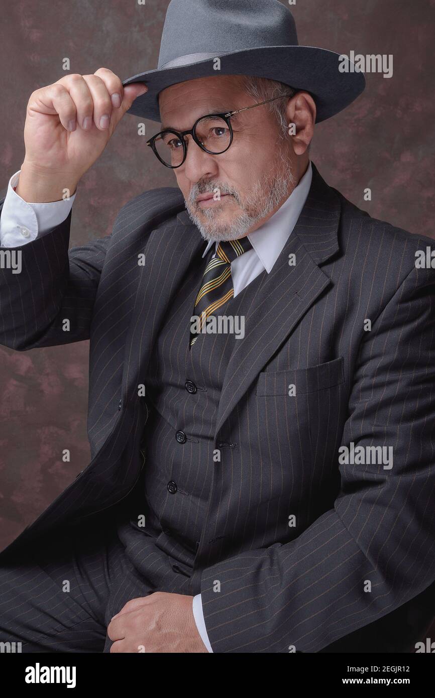 Un homme mûr posant pour la caméra dans une obscurité costume et chapeau à fines rayures marron Banque D'Images