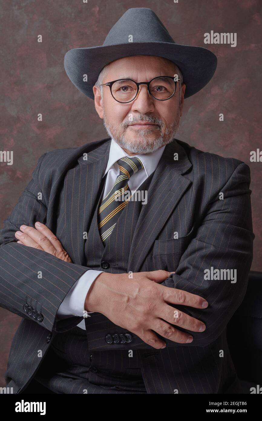 Un homme mûr posant pour la caméra dans une obscurité costume et chapeau à fines rayures marron Banque D'Images
