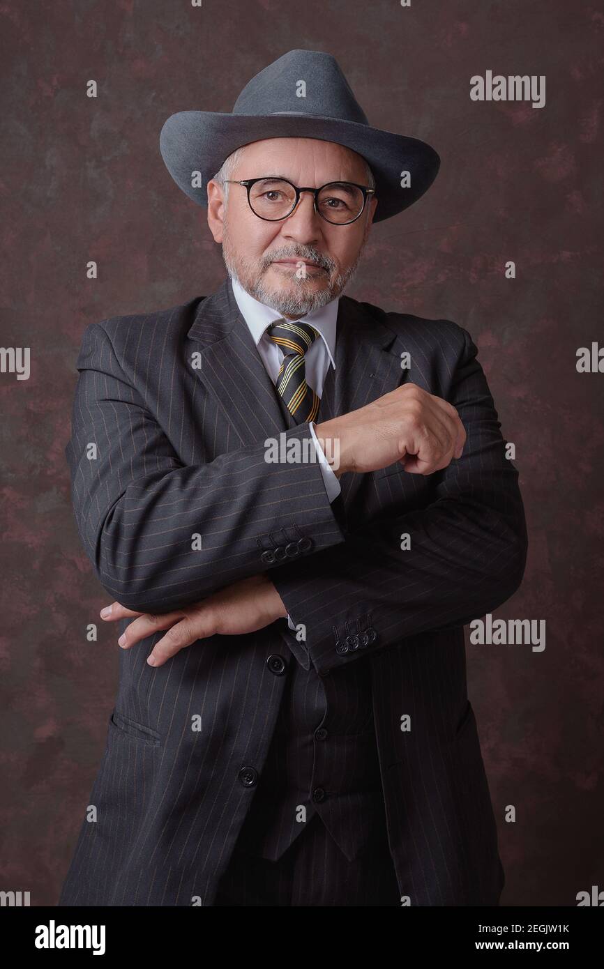 Un homme mûr posant pour la caméra dans une obscurité costume et chapeau à fines rayures marron Banque D'Images