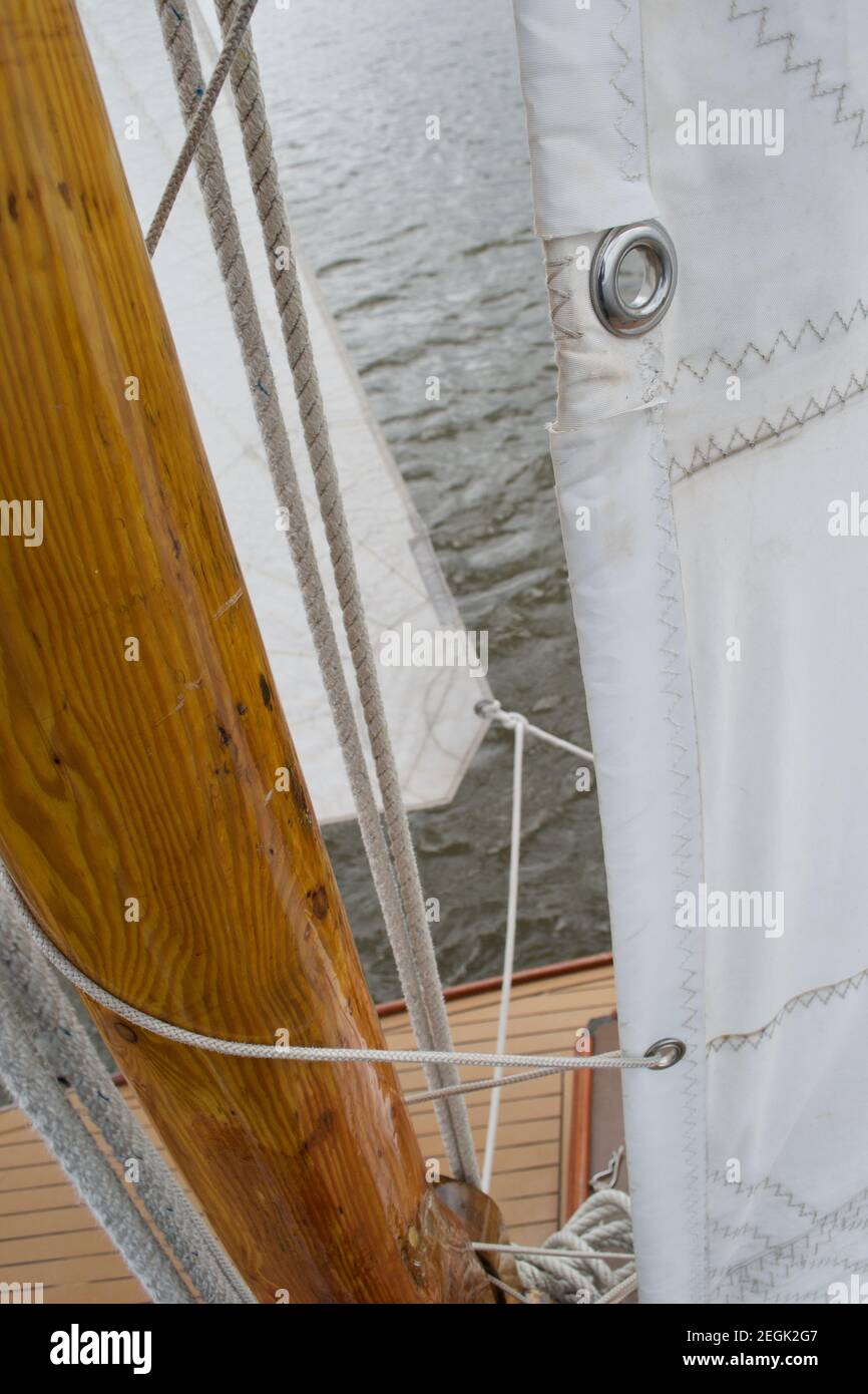 Détail d'une voile attachée au mât en bois d'un bateau à voile en cours d'afloat et sous la voile, naviguant au-dessus de l'eau grise.Œillets en tissu blanc, Banque D'Images