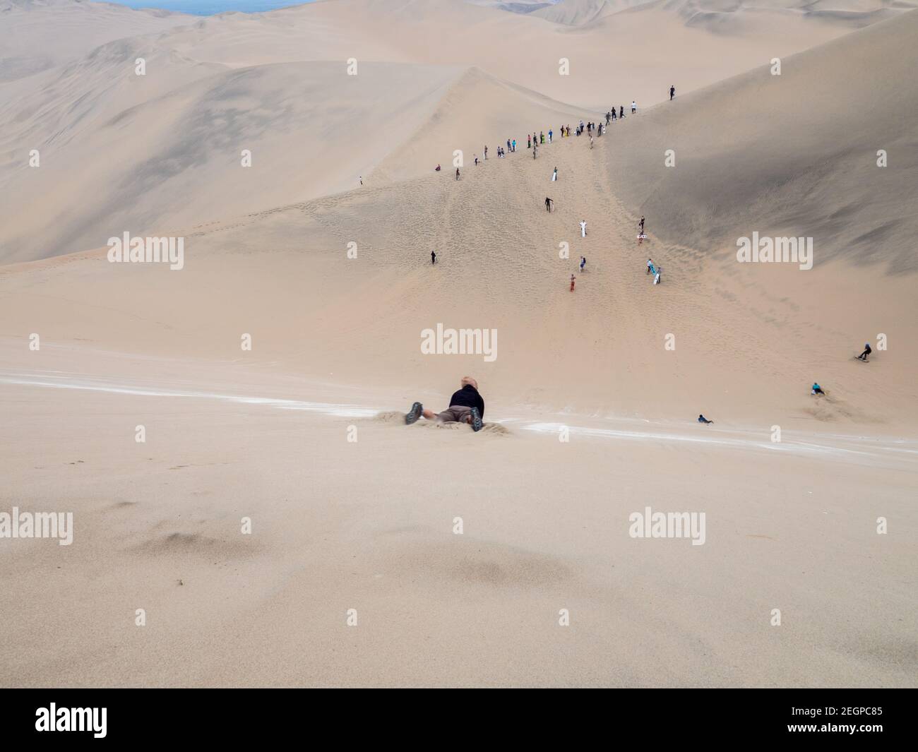 Les touristes glissent sur une dune de sable dans le désert de Huacachina au Pérou, de nombreux touristes attendent au fond Banque D'Images