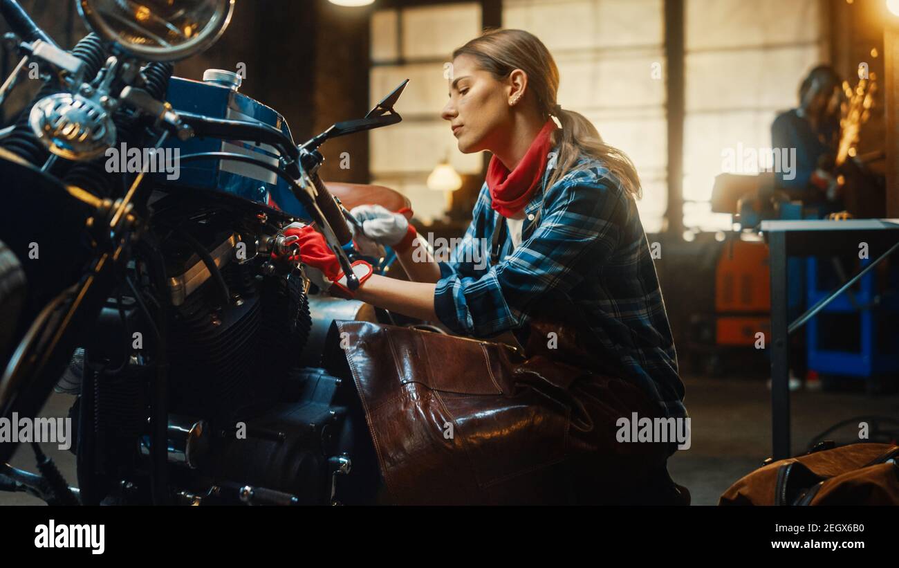 Jeune belle femme mécanicien travaille sur une moto Bobber personnalisée. Talentueuse Girl portant une chemise à carreaux et un tablier. Créatif authentique Banque D'Images