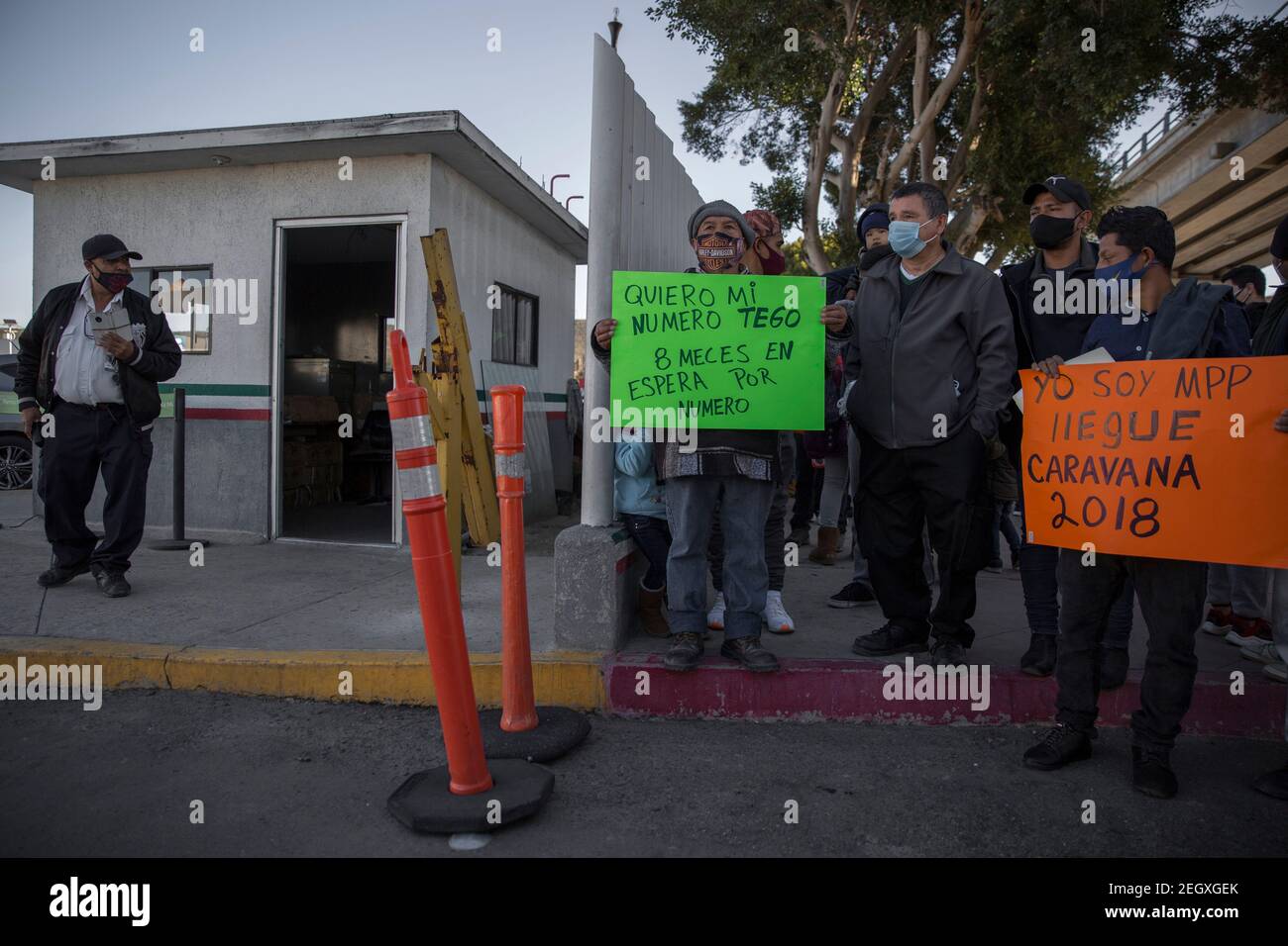 18 février 2021, Mexique, Tijuana : un agent de sécurité privé qui surveille le passage frontalier observe un groupe de migrants portant des signes de protestation. L'un des migrants (M) se plaint d'avoir attendu huit mois pour un rendez-vous avec les autorités américaines. Les migrants d'Amérique centrale et du Mexique réfugiés à l'abri d'Agape démontrés devant l'entrée principale du poste frontalier d'El Chaparral à la frontière entre Tijuana, au Mexique, Et San Diego, Californie, dans le but de demander aux autorités américaines d'ouvrir la frontière et de relancer le processus d'octroi de l'asile politique pour se réfugier Banque D'Images