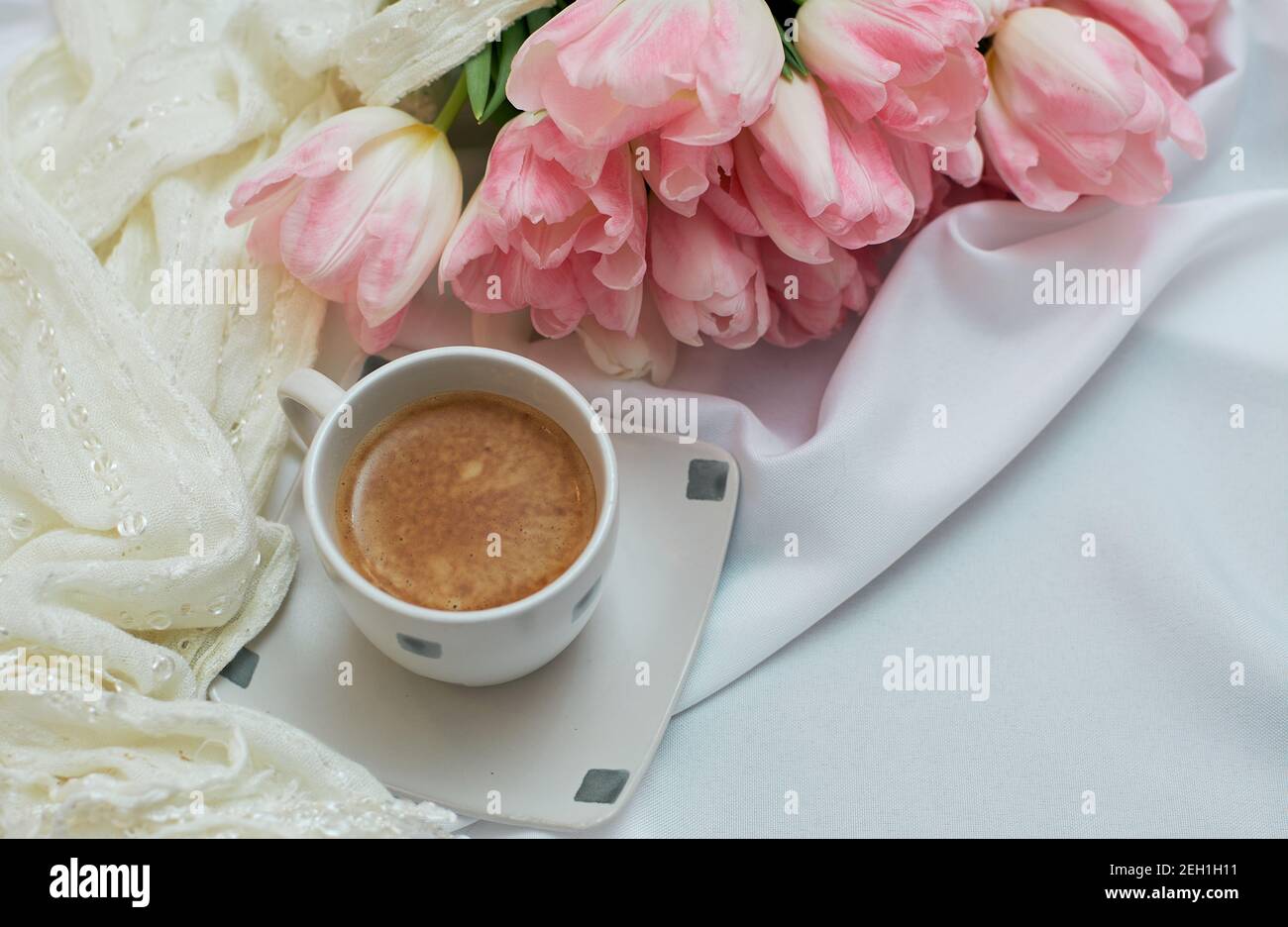 Café du matin aromatique dans une tasse blanche en céramique. Grand beau bouquet de tulipes de printemps. Banque D'Images