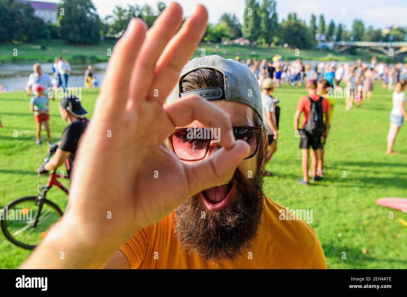 Homme visage gai regarde par geste ok. Homme barbu devant le fond de la foule au bord de la rivière. Réservez votre billet pour le festival d'été à l'avance. Assurez-vous de passer vos vacances d'été. Festival de visite Hipster. Banque D'Images