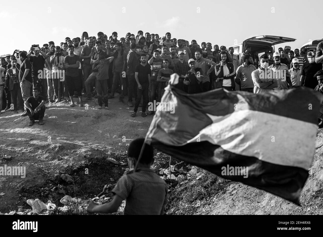 Un jeune garçon, le drapeau de la Palestine en main, passe devant une foule de gens qui regardent la manifestation. Ils seront utilisés pour créer une barrière de fumée et permettre à d'autres personnes de jeter des pierres sans être dérangés par le feu de sniper israélien... Les tensions sont vives le long de la frontière entre Gaza et Israël après plus d'un mois de manifestations de masse hebdomadaires près de la barrière qui a fait 50 morts parmi les manifestants palestiniens et plus de 1,700 blessés par des tirs militaires israéliens. Les dirigeants du Hamas à Gaza ont promis que les marches se poursuivront jusqu'à la levée du blocus israélien de dix ans du territoire. Manifestations ar Banque D'Images