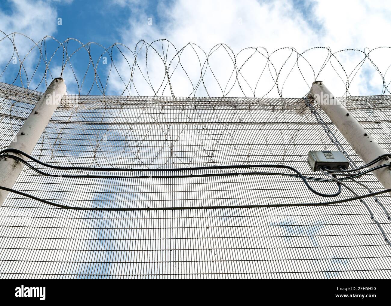 Clôture de prison de haute sécurité avec fil barbelé de rasoir sur le dessus en regardant depuis le sol à l'escrime en treillis métallique massif câbles et ciel bleu d'été liberté Banque D'Images