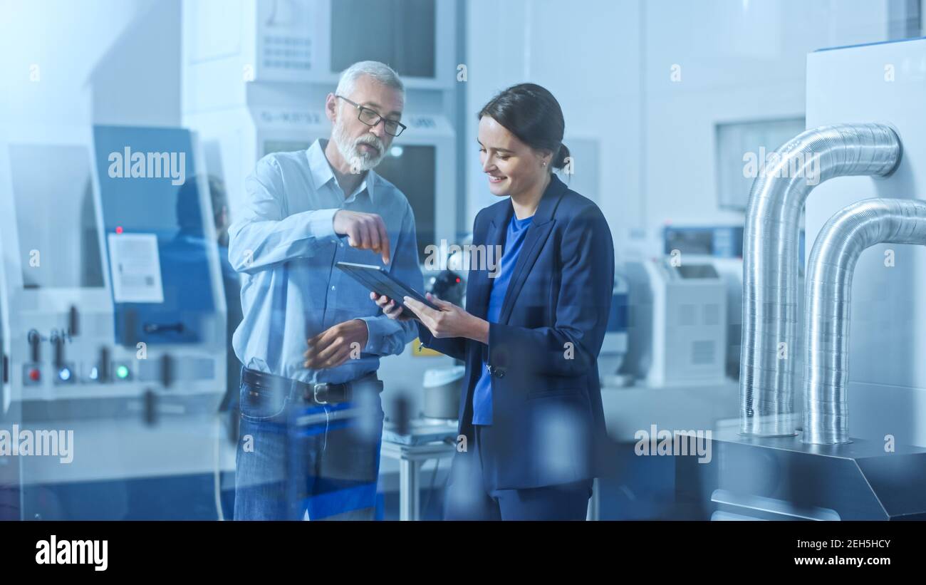 Usine moderne : Ingénieur féminin, responsable de projet masculin dans un centre de développement de haute technologie, parlant et utilisant un Tablet PC. Contemporain Banque D'Images