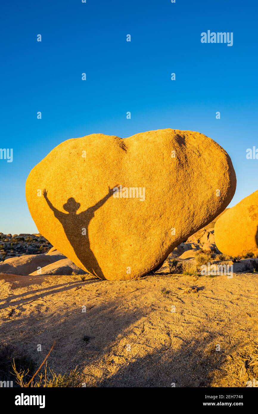 Bloc en forme de coeur avec ombre de l'homme avec les bras étirés. Dans la lumière du soir dorée au parc national de Joshua Tree, CA carte de Saint-Valentin approprié. Banque D'Images