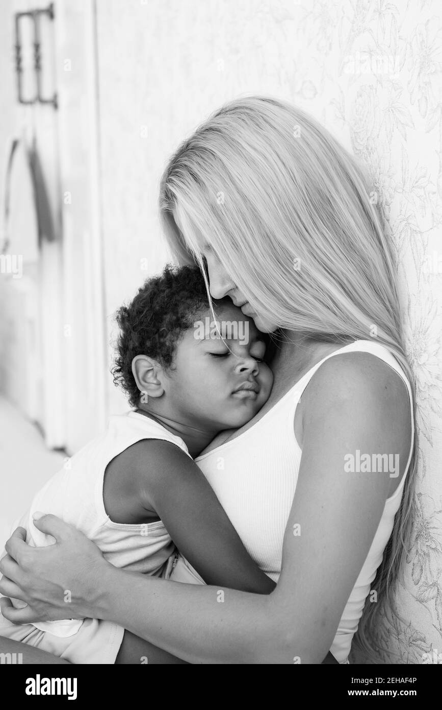 Portrait d'une jeune mère blanche blonde tenant, embrassant un petit fils afro-américain dans les bras. Le garçon appuya contre la poitrine des femmes. Sensibilité Banque D'Images
