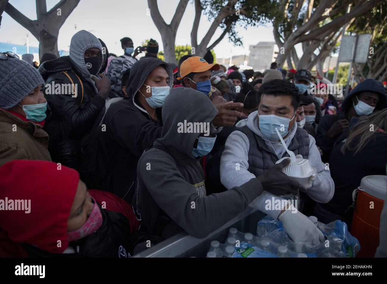 Tijuana, Mexique. 19 février 2021. Un homme portant un masque et des gants en latex distribue de la nourriture et de l'eau aux demandeurs d'asile en attente au passage frontalier « El Chaparral » au milieu de la pandémie de Corona. Suite à l’annonce d’un changement d’orientation de la politique migratoire des États-Unis, un grand nombre de migrants se sont rassemblés à la frontière entre le Mexique et les États-Unis. Crédit : Stringer/dpa/Alay Live News Banque D'Images