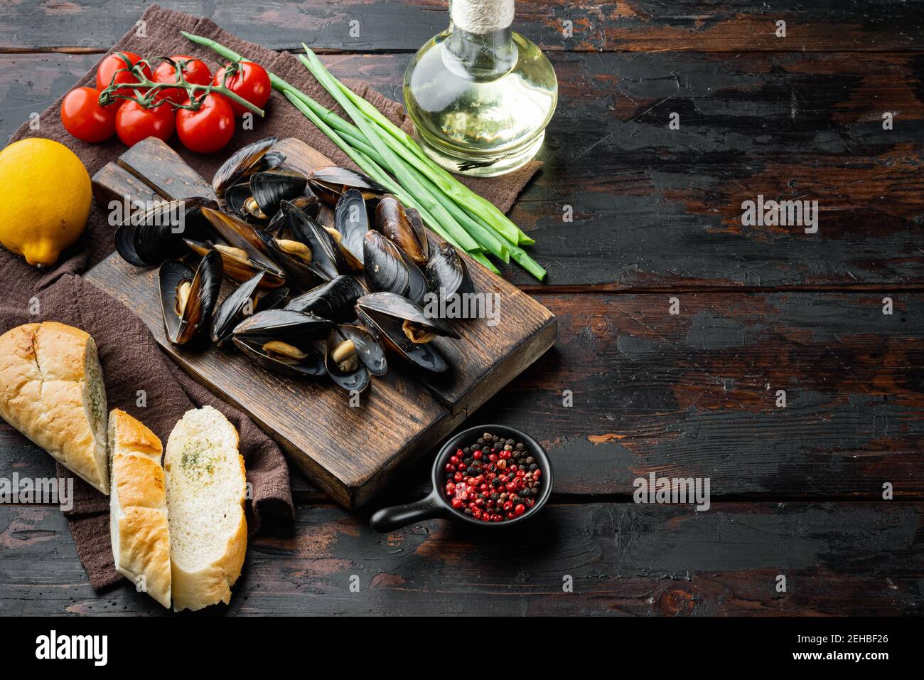 Moules cuites dans la sauce à l'ail avec le persil et l'ingrédient, sur la planche à découper en bois, sur le fond de la table en bois foncé, avec l'espace d'imitation et l'espace FO Banque D'Images