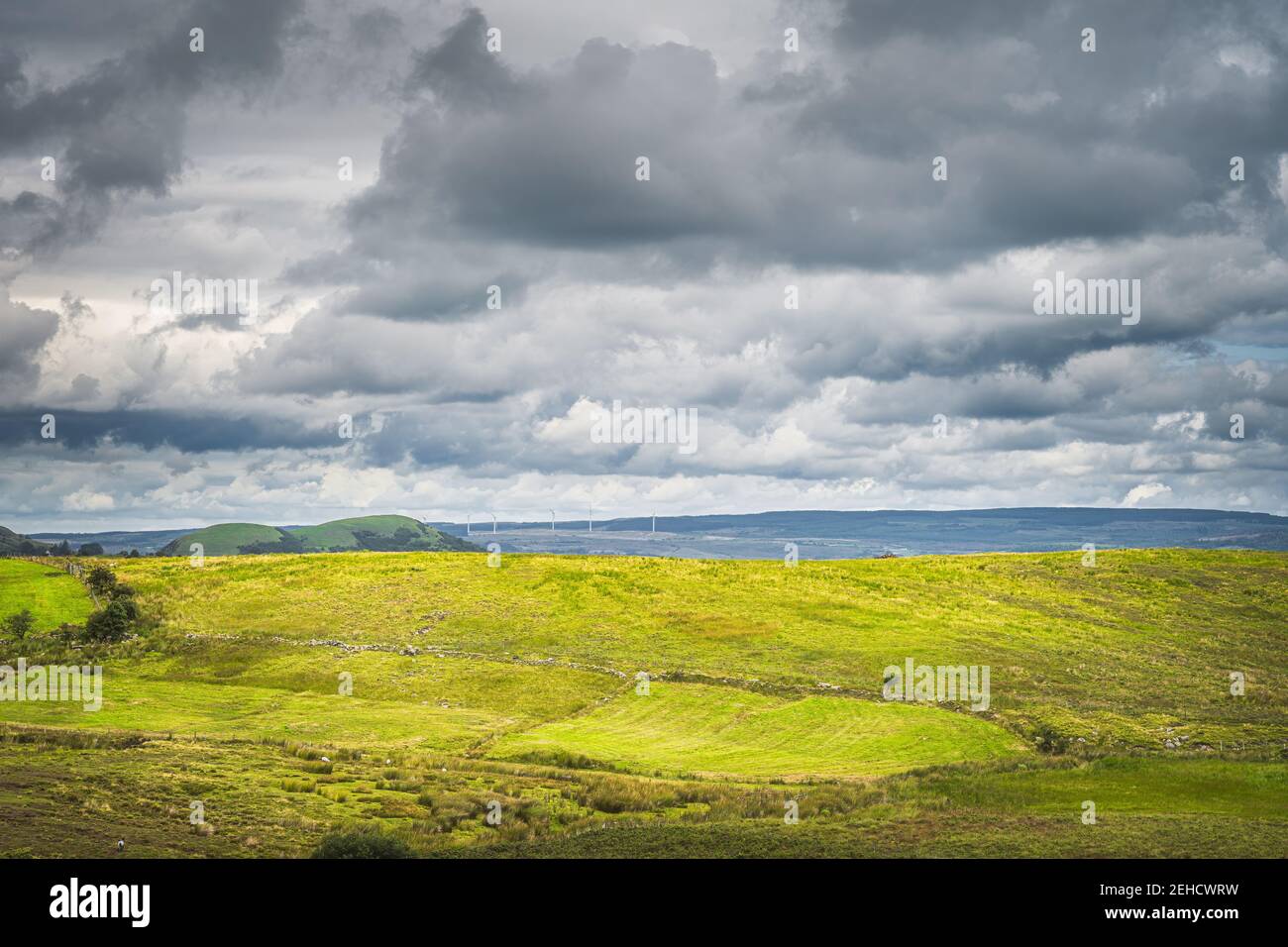 Colline verte avec pâturage et moutons illuminés par la lumière du soleil. Turbines électriques avec ciel orageux en arrière-plan, Cuilcagh Mountain Park, Irlande du Nord Banque D'Images