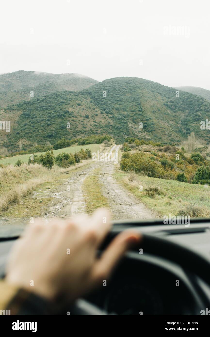 Crop anonyme mâle voiture de tourisme le long de la route rurale vide vers les collines vertes pendant le trajet Banque D'Images