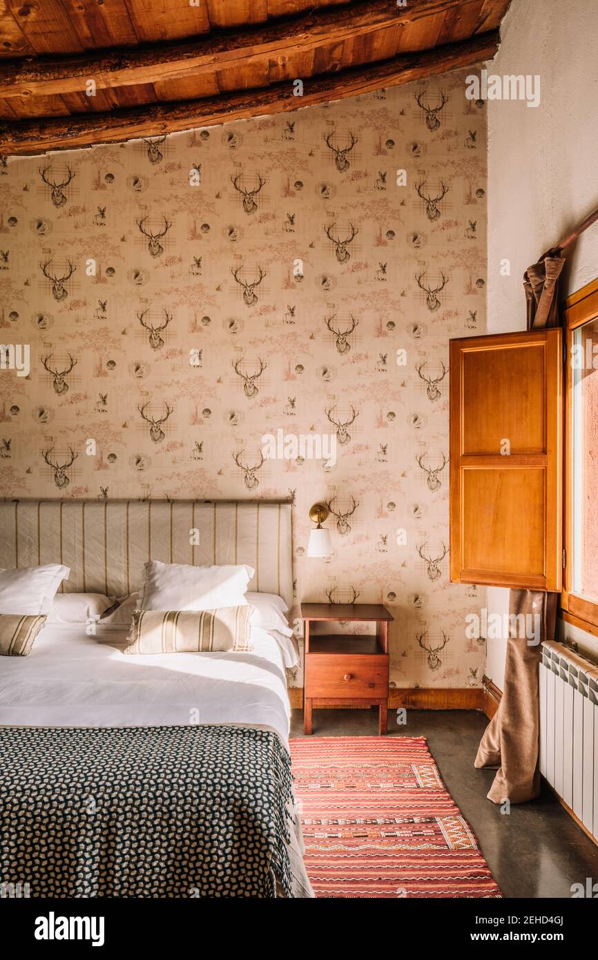 Intérieur d'une chambre élégante avec lit confortable recouvert d'un couvre-lit près de la fenêtre décorée de rideaux Banque D'Images