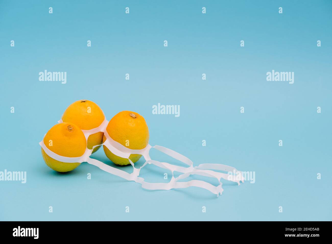 Citrons mûrs et juteux, entiers et brillants, entre un emballage en plastique fin anneaux avec trous Banque D'Images