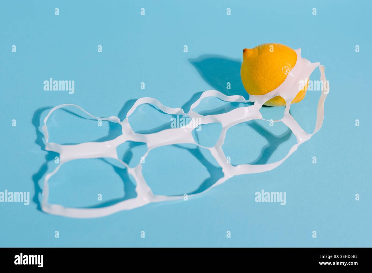 Citrons mûrs et juteux, entiers et brillants, entre un emballage en plastique fin anneaux avec trous Banque D'Images