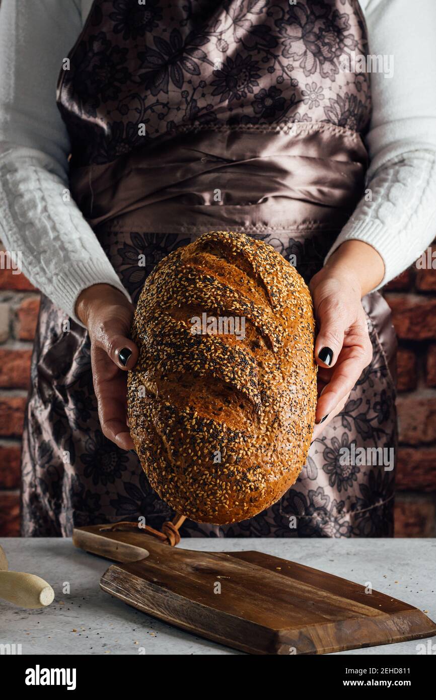 Crop anonyme femelle boulanger tenant le pain avec les graines de tournesol sur table dans le bakehouse Banque D'Images
