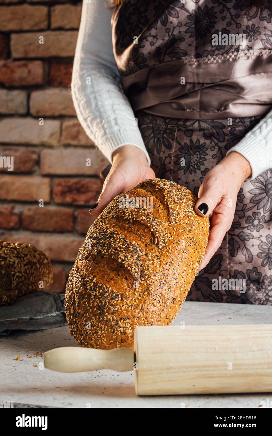 Crop anonyme femelle boulanger tenant le pain avec les graines de tournesol sur table dans le bakehouse Banque D'Images