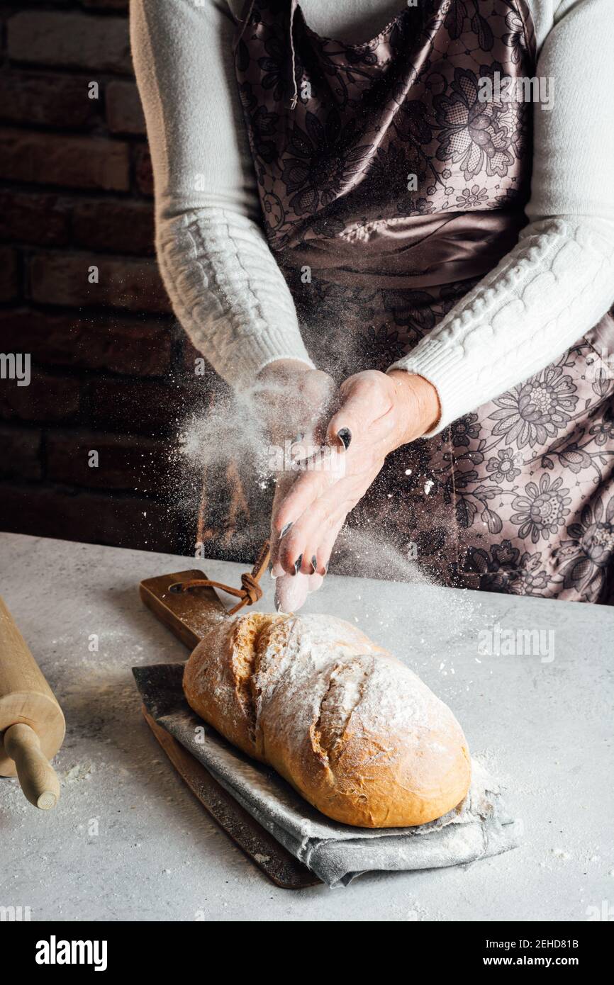 Crop anonyme femme artisan en tablier saupoudrer délicieux pain de pain blanc avec farine à la table dans le bakehouse Banque D'Images