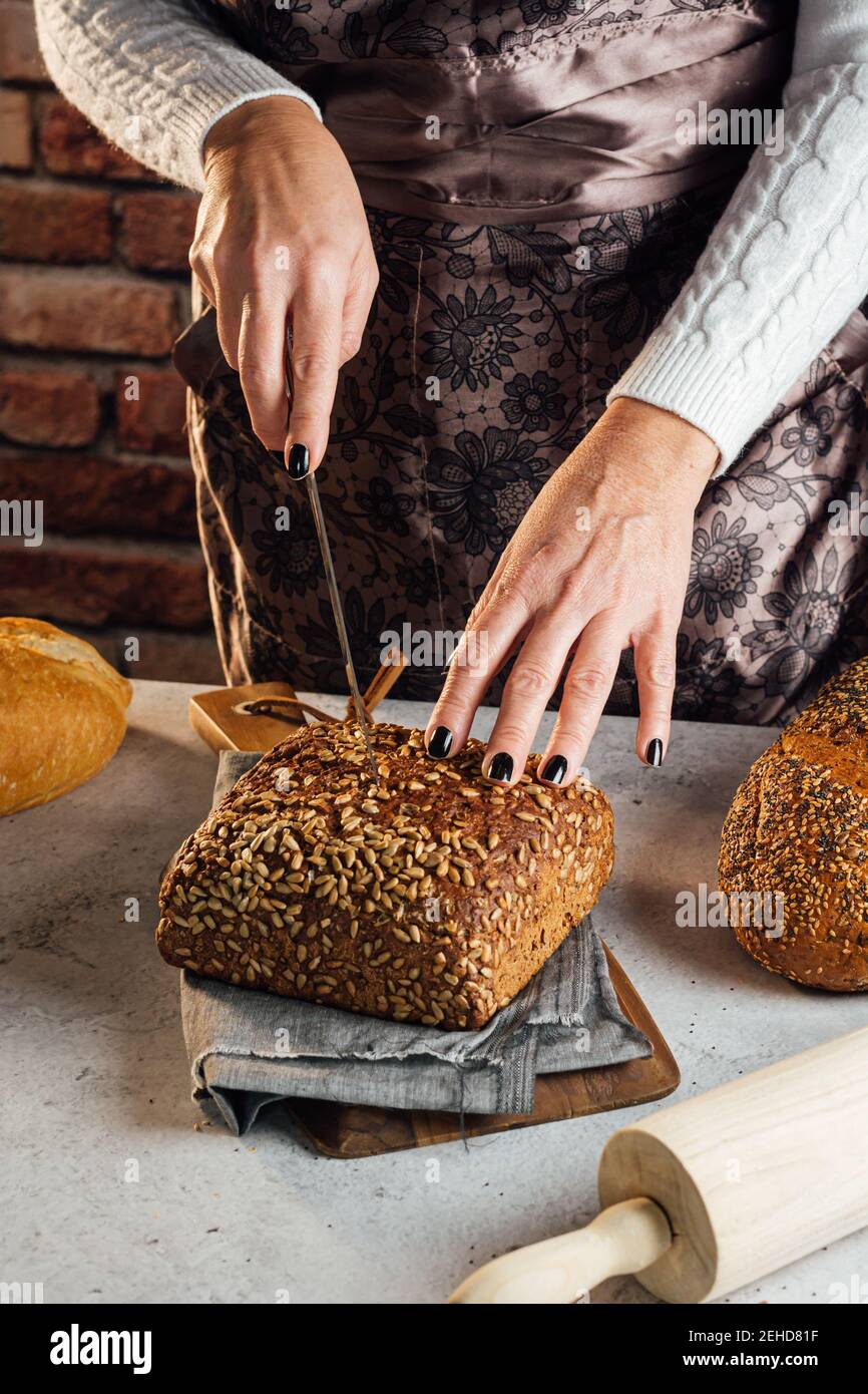Croise anonyme boulanger femelle avec couteau coupant pain de frais pain aux graines de tournesol sur la table dans le bakehouse Banque D'Images