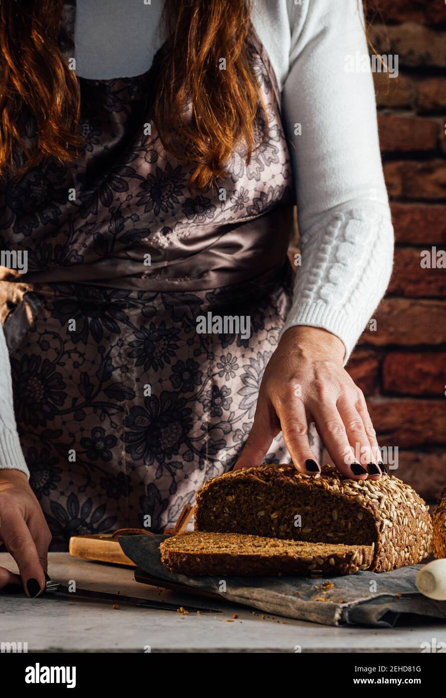 Croise anonyme boulanger femelle avec couteau coupant pain de frais pain aux graines de tournesol sur la table dans le bakehouse Banque D'Images