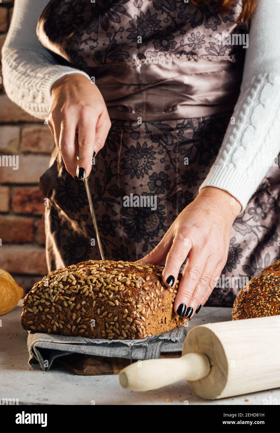 Croise anonyme boulanger femelle avec couteau coupant pain de frais pain aux graines de tournesol sur la table dans le bakehouse Banque D'Images