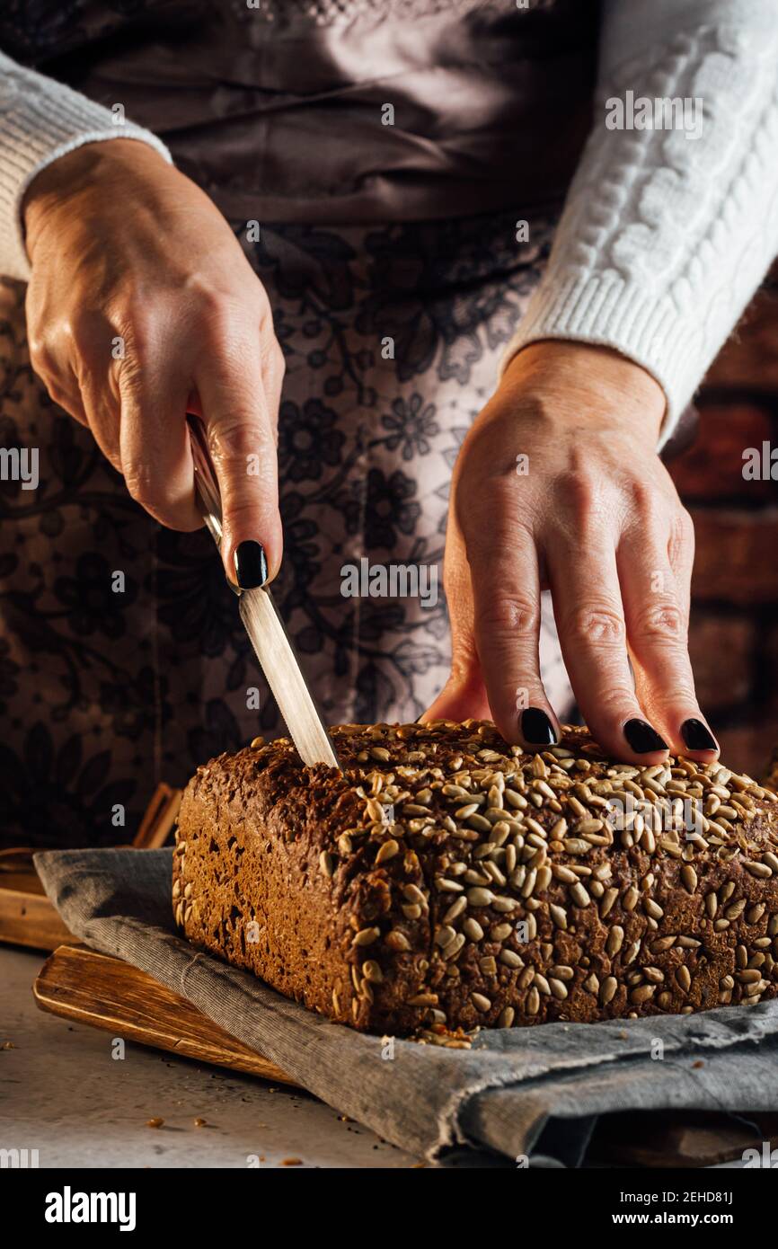 Croise anonyme boulanger femelle avec couteau coupant pain de frais pain aux graines de tournesol sur la table dans le bakehouse Banque D'Images