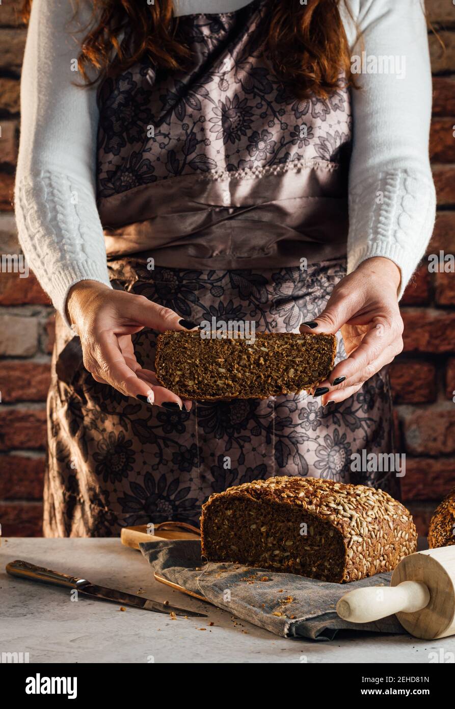 Croise anonyme boulanger femelle avec couteau coupant pain de frais pain aux graines de tournesol sur la table dans le bakehouse Banque D'Images