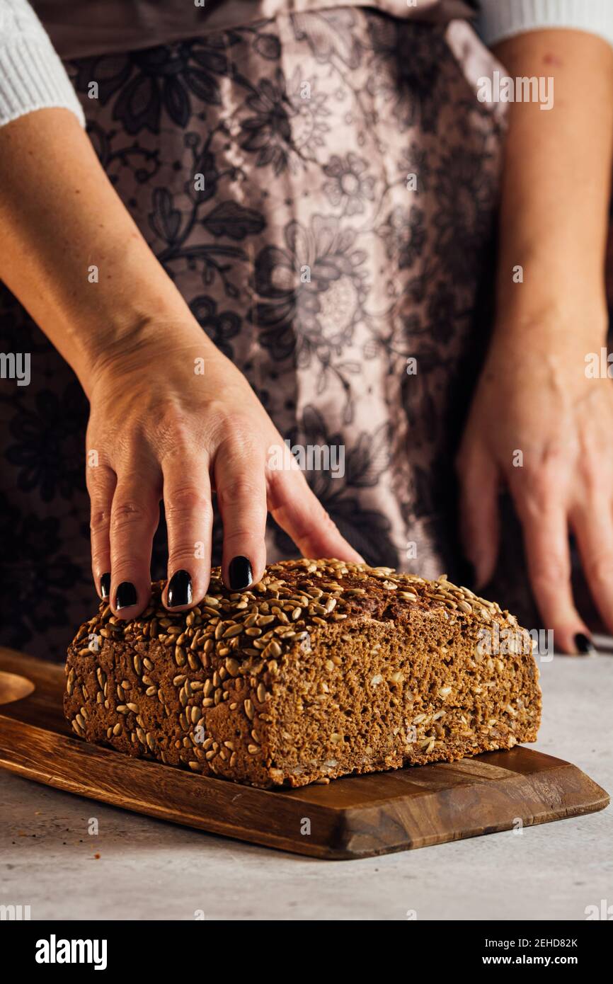 Crop anonyme femelle boulanger tenant le pain avec les graines de tournesol sur table dans le bakehouse Banque D'Images