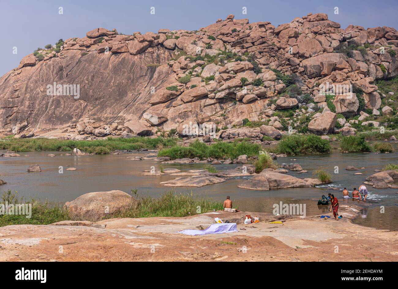 Anegundi, Karnataka, Inde - 9 novembre 2013 : île Navabrindavana. Les femmes et les hommes baignent dans la rivière Tungabhadra en face de la haute colline de rochers bruns et Banque D'Images