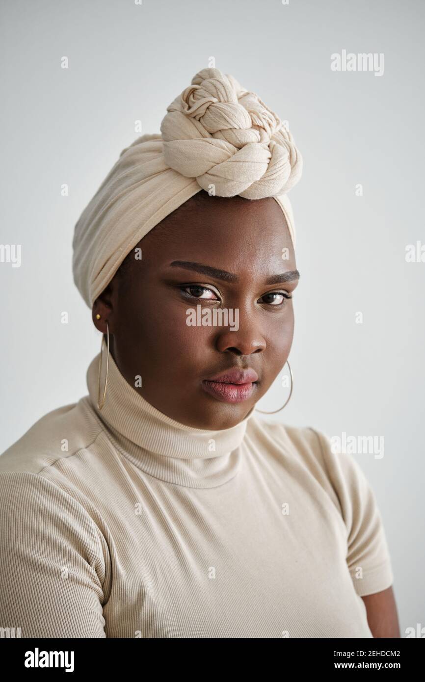 Magnifique jeune femme africaine en turban traditionnel élégant debout sur fond blanc et en regardant l'appareil photo Banque D'Images