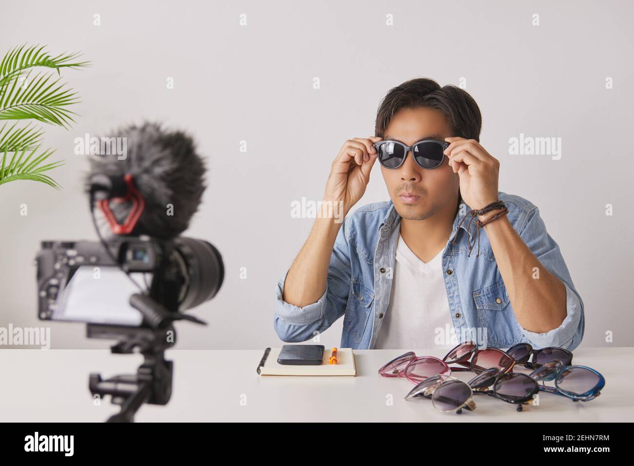 Vlogger asiatique ou Blogger en Jean chemises portent des lunettes de mode noires pour montrer au client tout en enregistrant la vidéo. Freelance Online Streaming avec Custo Banque D'Images