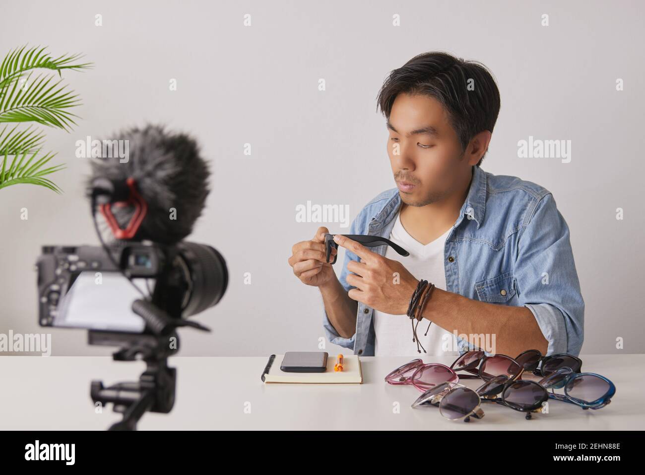 Avant gauche de l'asiatique vlogger ou Blogger dans Jean chemises examen mode lunettes par enregistrement vidéo. Freelance Online Streaming avec le client via Socia Banque D'Images