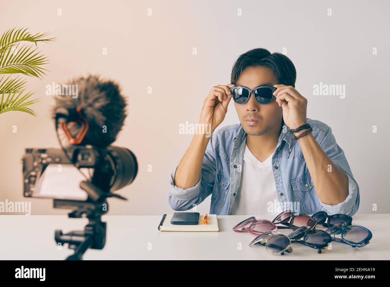 Vlogger asiatique ou Blogger en Jean chemises portent des lunettes de mode noires pour montrer au client tout en enregistrant la vidéo. Freelance Online Streaming avec Custo Banque D'Images