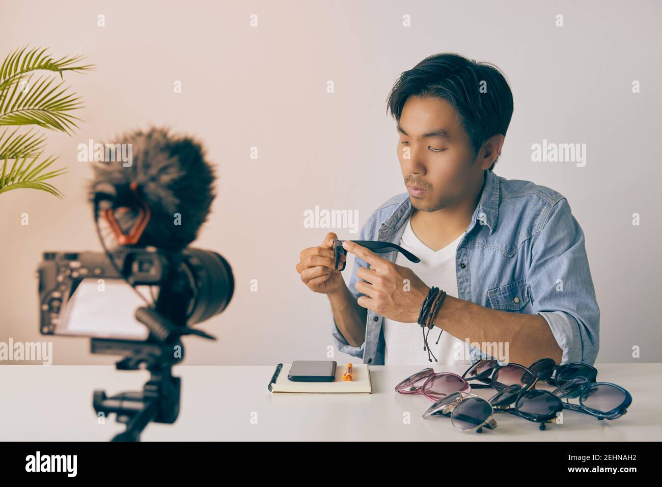 Avant gauche de l'asiatique vlogger ou Blogger dans Jean chemises examen mode lunettes par enregistrement vidéo. Freelance Online Streaming avec le client via Socia Banque D'Images