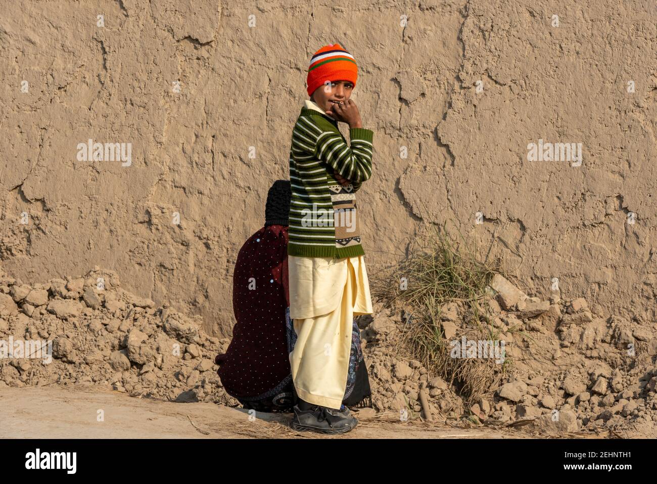 Village garçon debout devant un mur brun, Punjab, Pakistan Banque D'Images