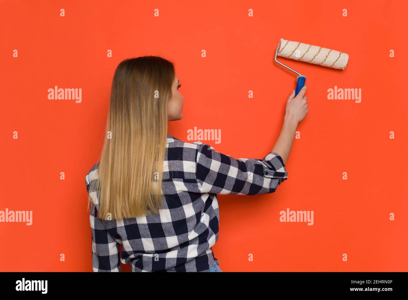 Jeune femme Blonde dans le maillot Lumberjack est peinture mur d'orange avec rouleau de peinture. Vue arrière. Prise de vue à la taille. Banque D'Images