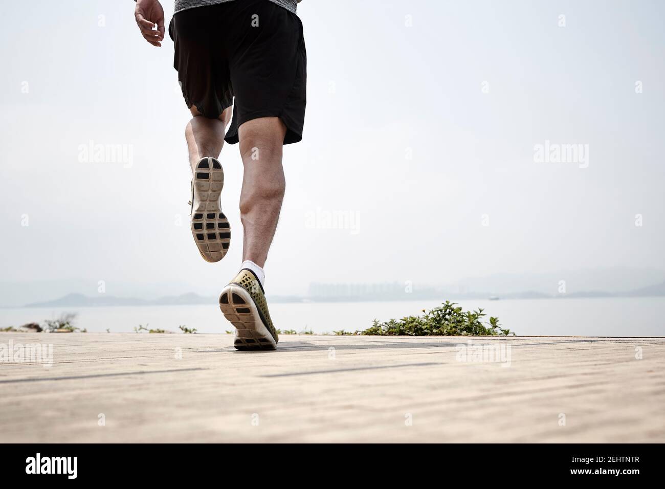 gros plan des jambes d'un coureur asiatique qui court au bord de la mer, vue arrière Banque D'Images