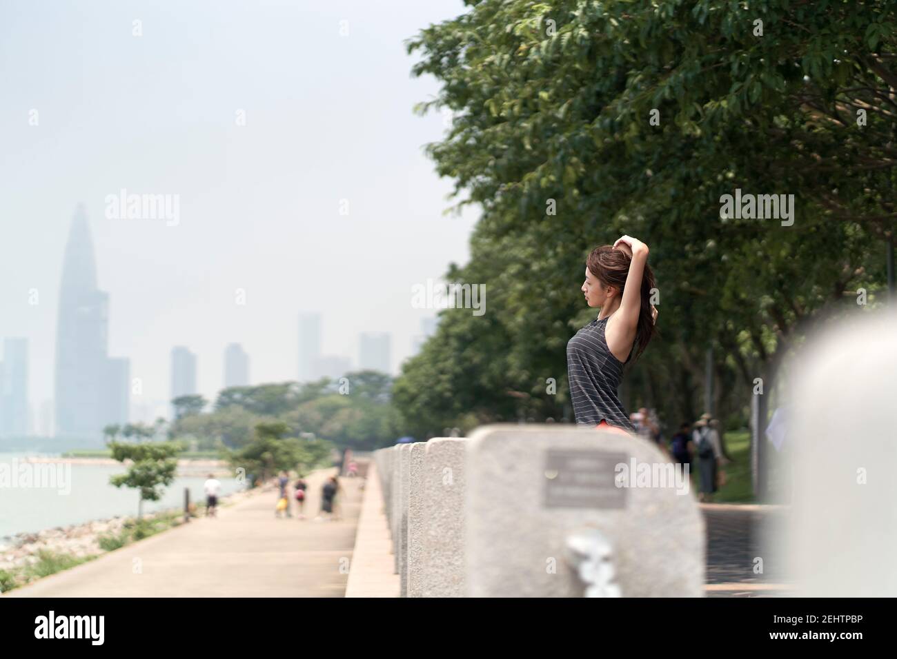 jeune femme asiatique en vêtements de sport s'échauffe avant de faire de l'exercice en plein air dans un parc en bord de mer Banque D'Images