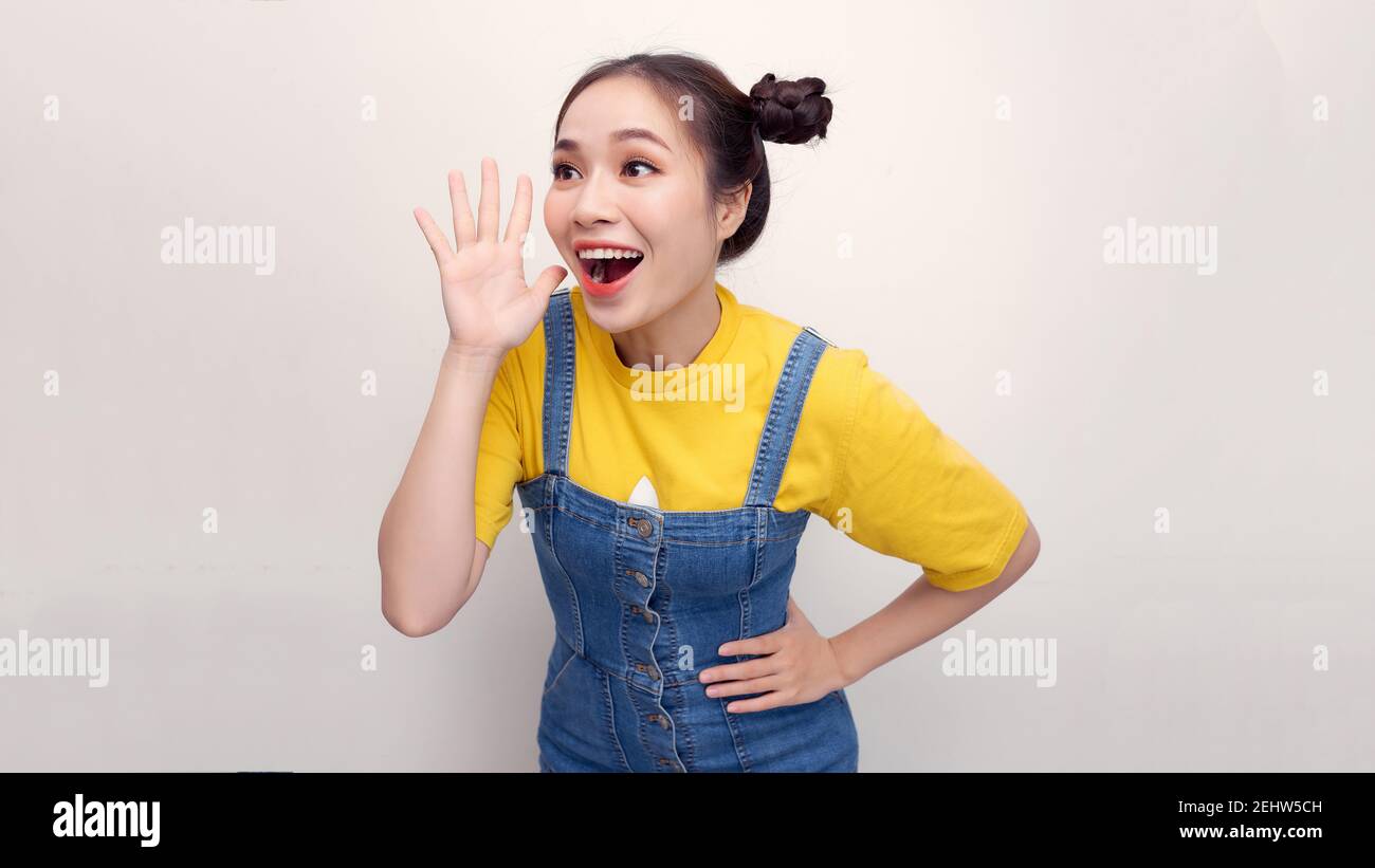 Portrait asiatique heureux belle jeune femme debout souriant profil criant et en tenant la main près de sa bouche ouverte sur fond blanc Banque D'Images