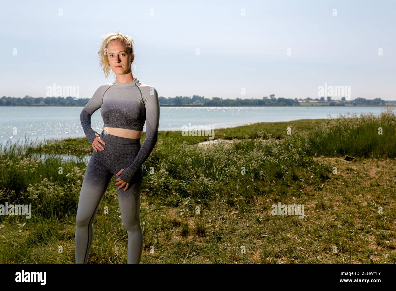 Belle tenue jeune femme en sport prêt à l'entraînement au soleil sur la rive de la rivière. Concept de mode de vie sain Banque D'Images