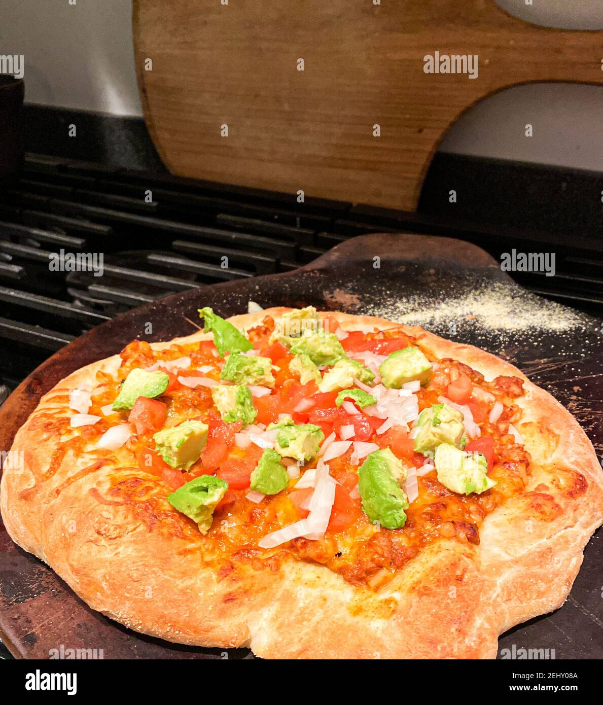 Une pizza maison mexicaine juste à l'extérieur du four avec avocat vert sur le dessus reposant sur une pierre de pizza sur une cuisinière. Banque D'Images